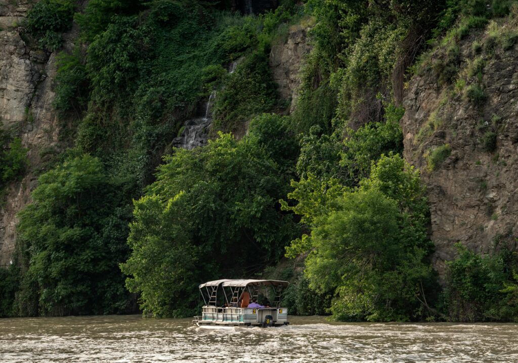 A serene boat journey along the cliffs of Tbilisi river, surrounded by lush greenery.