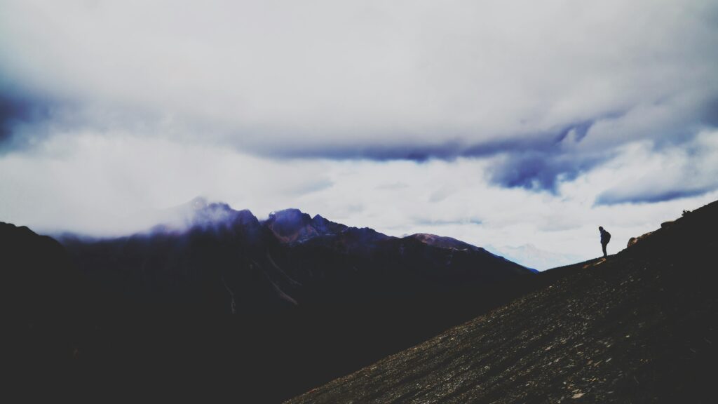 A lone hiker silhouetted against dramatic mountain landscape at dusk in Alberta, Canada.